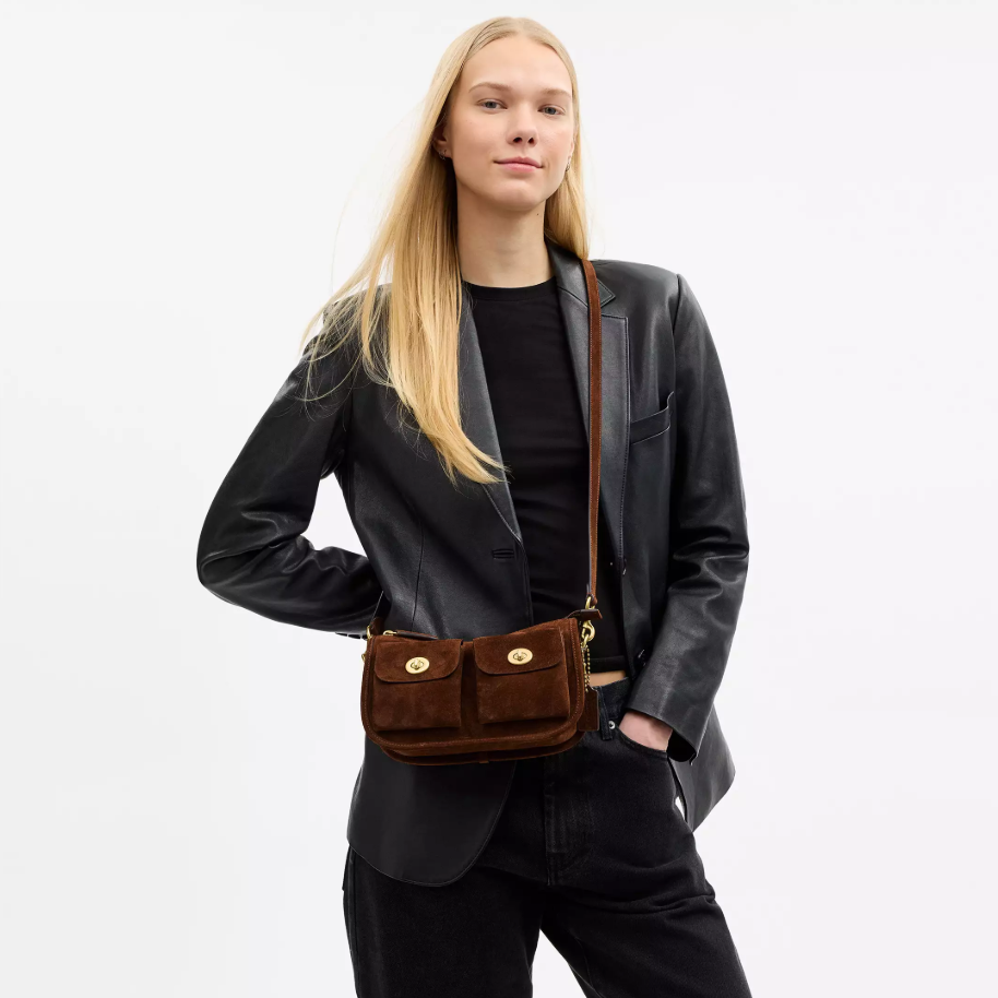 Person wearing a black blazer and carrying a brown leather bag on a white background